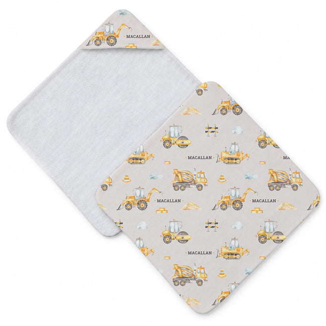 Baby hooded towel featuring yellow construction vehicles, traffic cones, bricks, blue clouds, and the name Macallan in gray lettering.