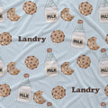 A light blue fabric with a repeating pattern of brown chocolate chip cookies, milk bottles, and the word 'Landry' in brown text.