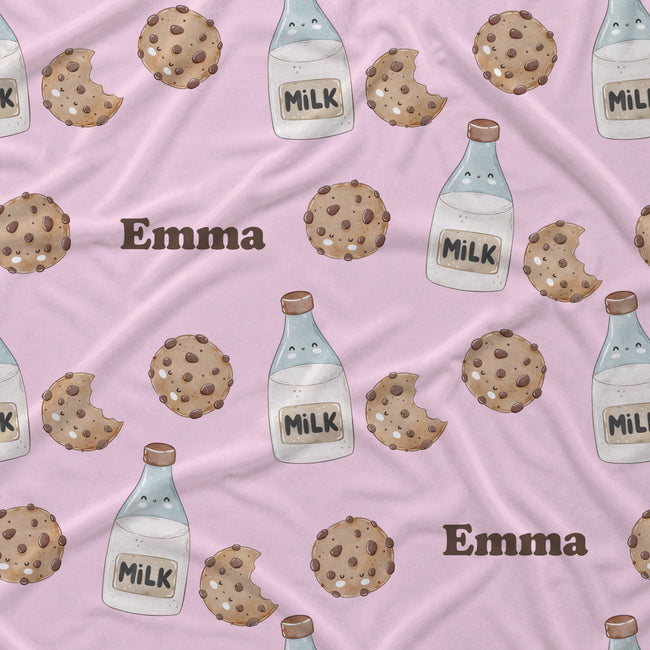 A close-up of a pink fabric with a repeating pattern of chocolate chip cookies, milk bottles, and the name 'Emma' in brown text.