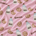 Pink satin fabric with a repeating watercolor pattern of chocolate chip cookies, milk bottles, and the name 'Emma' in brown text.