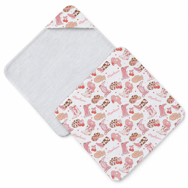 White hooded towel with pink cowgirl boots, Western hats, bows, cherries, hearts, and the name Marlowe in pink script.