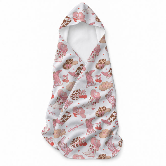 White hooded towel with pink cowgirl boots, Western hats, bows, cherries, hearts, and the name Marlowe in pink script.