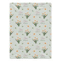 Pale sage blanket with white narcissus flowers, golden-orange centers, green leaves, and the name Clara Noelle in rose and green.