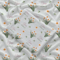 Pale sage swaddle blanket with white narcissus flowers, scattered green leaves, and the name Clara Noelle repeated in rose and green.