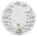 A round baby growth chart blanket featuring a white background, gray watercolor clouds, small gold stars, a cute green dinosaur at the bottom, and black numbers 1 through 12 arranged in a circular pattern around the center, with the word 'months' printed below the dinosaur.