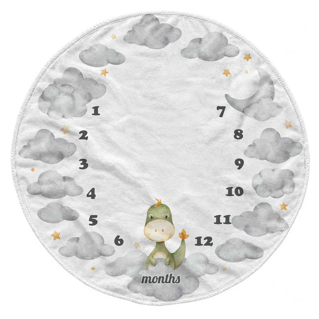 A round baby growth chart blanket featuring a white background, gray watercolor clouds, small gold stars, a cute green dinosaur at the bottom, and black numbers 1 through 12 arranged in a circular pattern around the center, with the word 'months' printed below the dinosaur.
