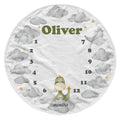 A round baby milestone chart towel or blanket featuring a white background with gray watercolor clouds, a small green dinosaur, the name 'Oliver' in olive green, and numbers 1 through 12 arranged around the circle with the word 'months' at the bottom.