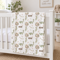 A personalized baby blanket with a dinosaur and balloon pattern draped over a white wooden crib in a bright nursery setting.