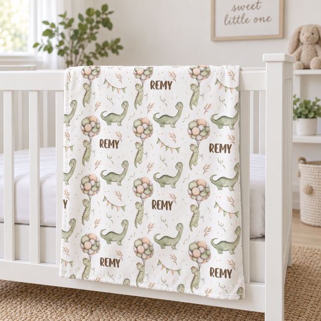A personalized baby blanket with a dinosaur and balloon pattern draped over a white wooden crib in a bright nursery setting.