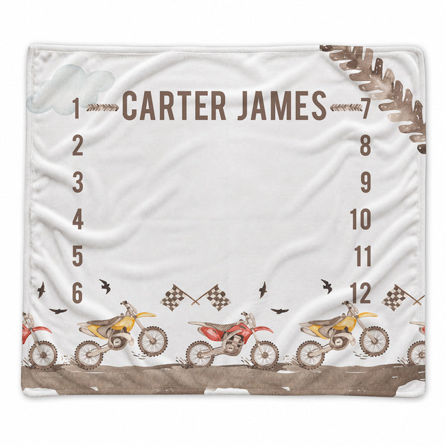 A white personalized blanket featuring a dirt bike race theme, with the name 'CARTER JAMES' printed at the top, numbered positions 1 through 12, and illustrations of dirt bikes along the bottom.
