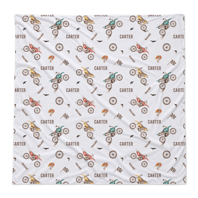 A square white baby swaddle blanket featuring a repeating pattern of vintage dirt bikes, checkered flags, racing flags, and the brand name 'CARTER' printed in brown.
