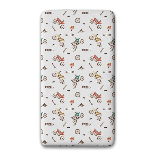 A twin fitted sheet featuring a repeating pattern of vintage-style dirt bikes, racing helmets, and the name 'CARTER' printed in brown on a light gray background.