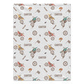 A rectangular white blanket featuring a repeating pattern of vintage dirt bikes, checkered flags, birds, and the name 'CARTER' printed in brown.