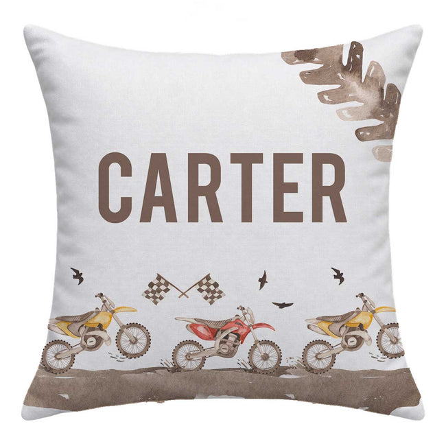 A square throw pillow with a custom printed design featuring the name 'CARTER' in large brown letters, three dirt bikes in yellow, red, and yellow, and brown tire tracks on a light gray background.