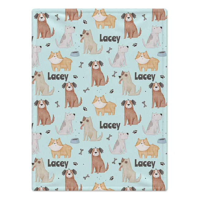 A personalized dog blanket featuring a repeating pattern of various cartoon dog illustrations, paw prints, bones, and the name 'Lacey' on a light blue background.