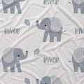 A close-up of a white fabric with a repeating pattern of gray cartoon elephants, gray leaves, and the word 'river' in gray lowercase letters.