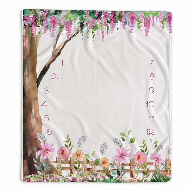 Enchanted Garden baby girl milestone blanket with hanging pink blossoms, a watercolor tree, flowers, and numbers 1–12.