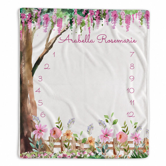 Enchanted Garden baby girl milestone blanket with Arabella Rosemarie, hanging pink blossoms, a watercolor tree, flowers, and numbers 1–12.