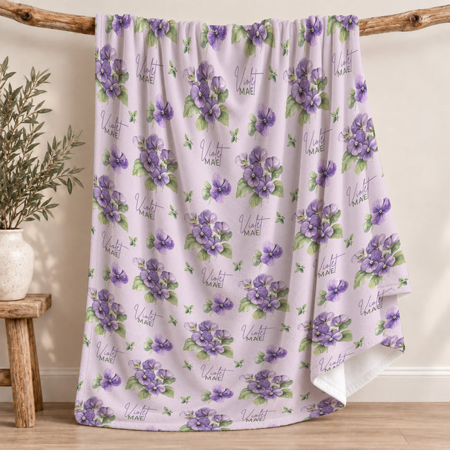Pale lavender blanket with purple violet flowers, green leaves, and the name Violet Mae in purple script and green lettering.