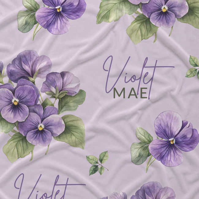 Pale lavender fabric with purple violet flowers, green leaves, and the name Violet Mae in purple script and green lettering.