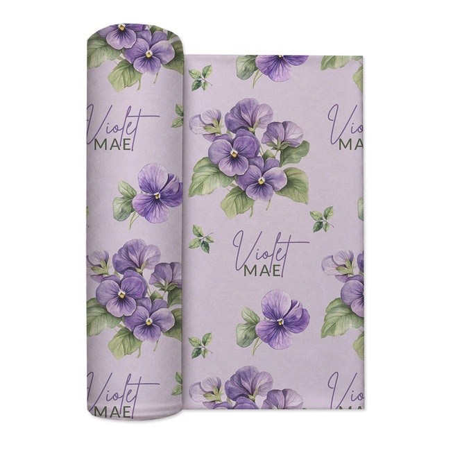Pale lavender swaddle blanket with purple violet flowers, green leaves, and the name Violet Mae in purple and green lettering.