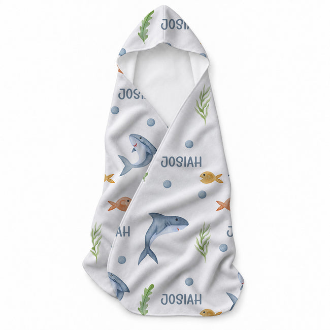 White hooded towel featuring blue sharks, yellow and orange fish, green seaweed, blue bubbles, and the name Josiah.