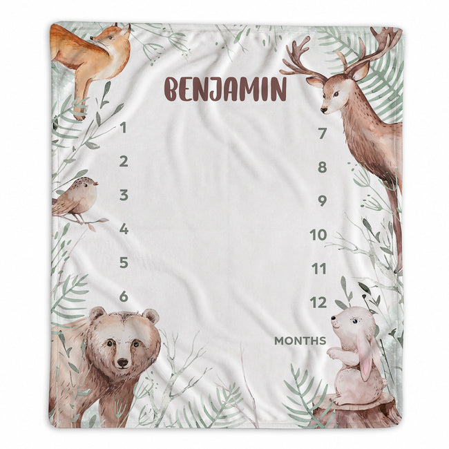 A personalized baby monthly milestone blanket featuring woodland animal illustrations including a deer, bear, rabbit, bird, fox, and leaves. The center is blanked out with the name 'BENJAMIN' and columns for 1 through 12 months with the label 'MONTHS'.