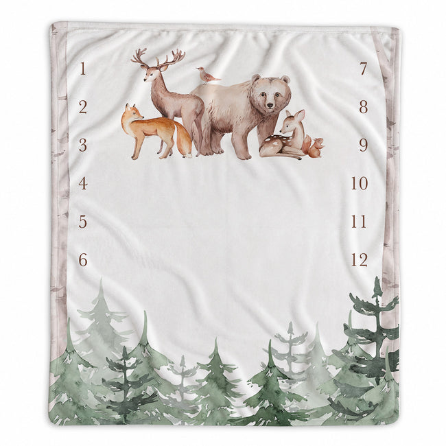 A baby milestone blanket with a woodland theme, featuring watercolor-style illustrations of a bear, deer, fox, bird, and pine trees. The center is blank with printed numbers 1 through 12 arranged vertically on both sides.