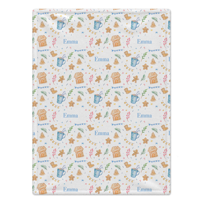 A square fabric item, likely a tea towel or blanket, featuring a festive gingerbread house pattern on a white background. The design includes the name 'Emma' in blue, decorated with blue mugs, brown gingerbread houses, and small green leaves.
