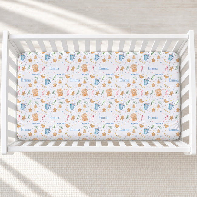 A fitted crib mattress with a whimsical pattern of teddy bears, stars, stars, and the name 'Emma' in blue, shown inside a white wooden crib.