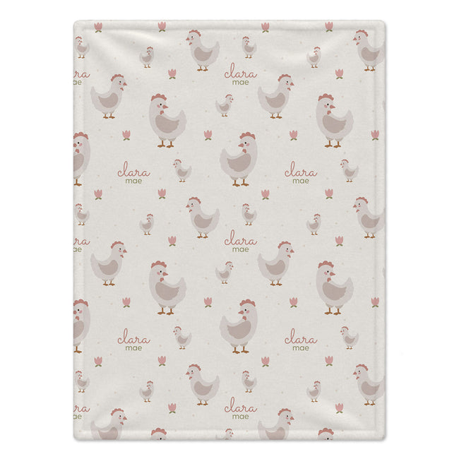 A square fabric item, likely a baby blanket or towel, featuring a repeating pattern of cartoon chickens and the names 'clara' and 'mae' in a soft pink font on a light beige background.