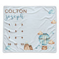 A personalized milestone blanket featuring a fun watercolor hot air balloon design with clouds in a light blue color