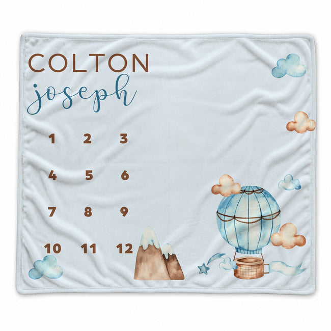 A personalized milestone blanket featuring a fun watercolor hot air balloon design with clouds in a light blue color