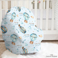A baby car seat cover with a light blue background and a watercolor print of hot air balloons, stars, and clouds, personalized with the name 'COLTON joseph'. The baby car seat cover is displayed on a white wooden baby crib in a nursery setting.