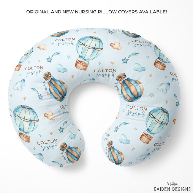 Personalized U-shaped nursing pillow cover featuring a light blue background with a watercolor hot air balloon pattern and the text 'COLTON joseph' printed on it. The pillow is displayed on a clean white background with promotional text at the top and the brand logo 'CAIDEN DESIGNS' at the bottom right.