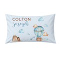 A personalized light blue pillowcase featuring watercolor-style illustrations of a hot air balloon, clouds, mountains, and the names 'COLTON' and 'joseph' in brown and blue lettering.
