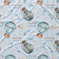 Light blue fabric with a repeating pattern of watercolor hot air balloons, stars, clouds, and the personalized name 'COLTON joseph' in brown and blue lettering.