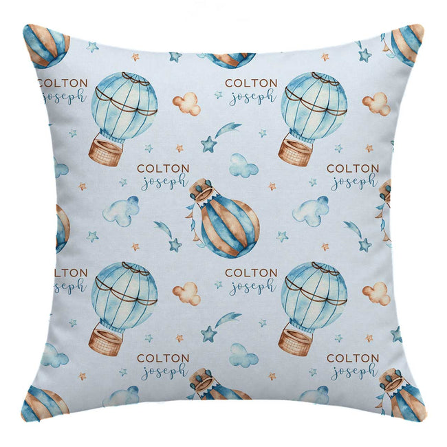 A square throw pillow featuring a light blue watercolor print of hot air balloons, clouds, stars, and the personalized name 'COLTON joseph' repeated across the front.