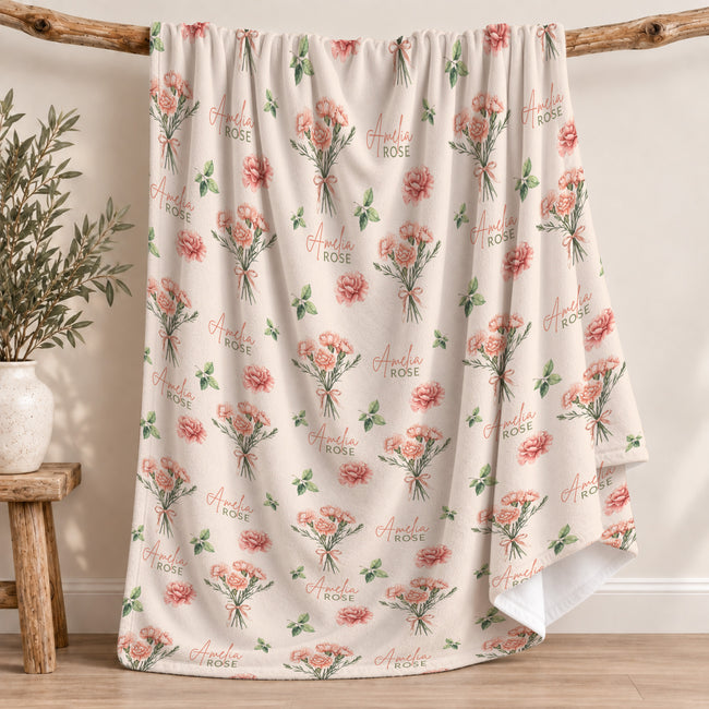 Cream blanket with peach-pink carnation bouquets, green leaves, and the name Amelia Rose in coral and green lettering.