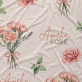 Cream fabric with peach-pink carnation bouquets, green leaves, and the name Amelia Rose in coral and green lettering.