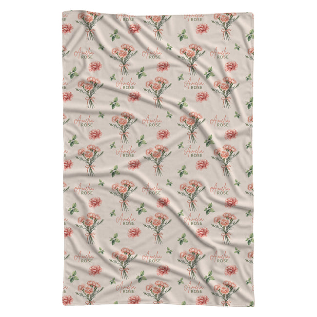 Cream swaddle blanket with peach-pink carnation bouquets, green leaves, and the name Amelia Rose in coral and green lettering.