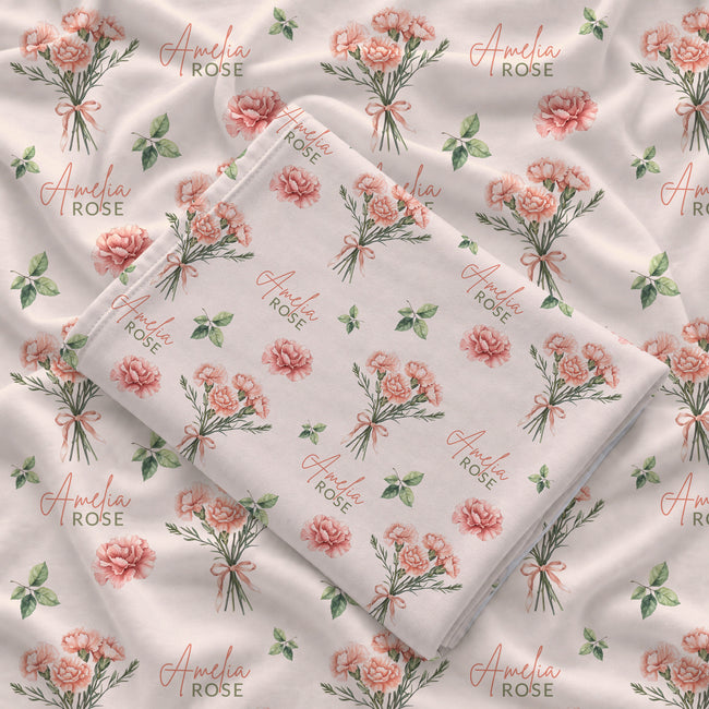 Cream swaddle blanket with peach-pink carnation bouquets, green leaves, and the name Amelia Rose in coral and green lettering.