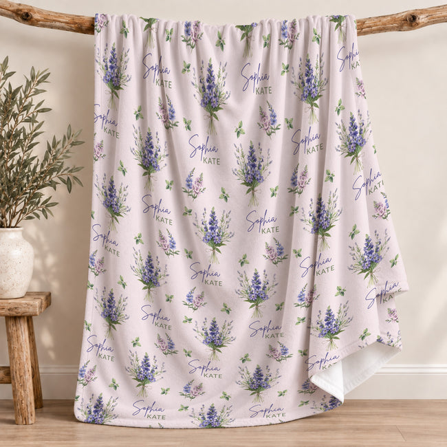 Pale blush blanket with blue and lavender larkspur bouquets, green leaves, and the name Sophia Kate in blue and green lettering.