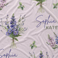 Personalized fabric featuring a watercolor floral pattern with purple and lavender bouquets, green leaves, and the names 'Sophia' and 'KATE' printed on a light blush pink background.