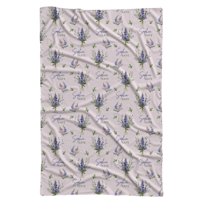 Pale blush swaddle blanket with blue and lavender larkspur bouquets, green leaves, and the name Sophia Kate in blue and green.