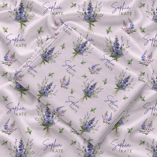 Pale blush swaddle blanket with blue and lavender larkspur bouquets, green leaves, and the name Sophia Kate in blue and green.