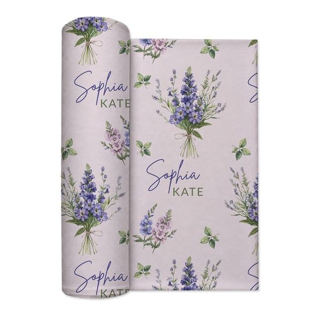 Pale blush swaddle blanket with blue and lavender larkspur bouquets, green leaves, and the name Sophia Kate in blue and green.