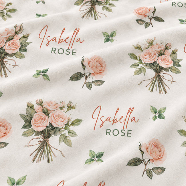 A close-up of a cream-colored fabric with a repeating pattern of pink rose bouquets, green leaves, and the personalized text 'Isabella ROSE' in cursive and block lettering.
