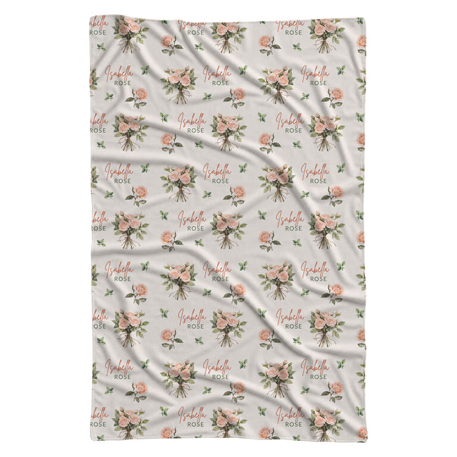 Ivory swaddle blanket with peach rose bouquets, scattered green leaves, and the name Isabella Rose in coral and green lettering.
