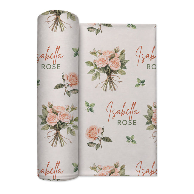 Ivory swaddle blanket with peach rose bouquets, scattered green leaves, and the name Isabella Rose in coral and green lettering.